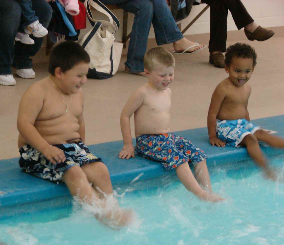 Three children sitting on the edge of a pool